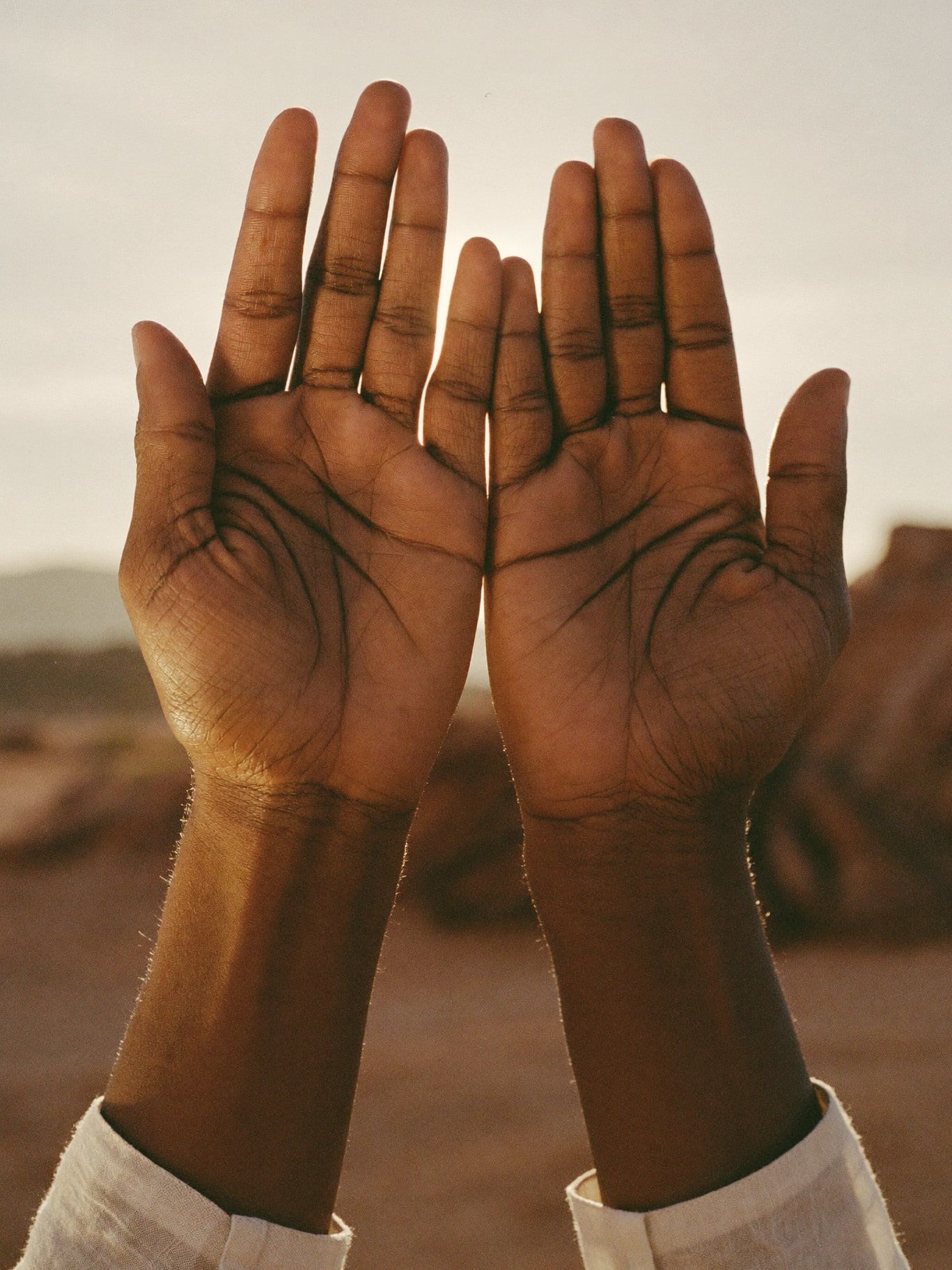 Two hands held apart, backlit by the setting sun over the desert