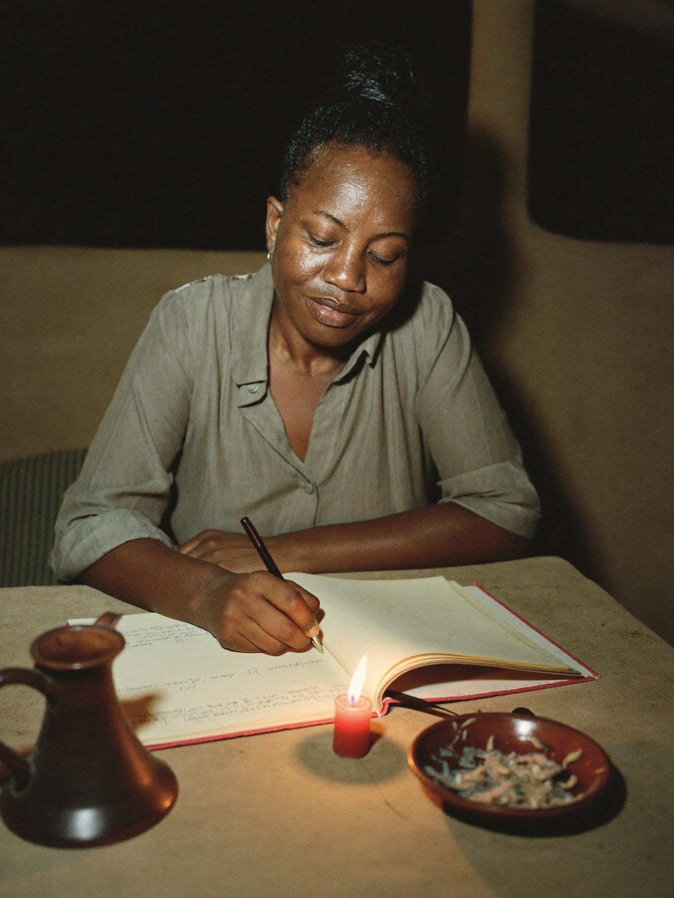 A woman writing in a notebook by candlelight