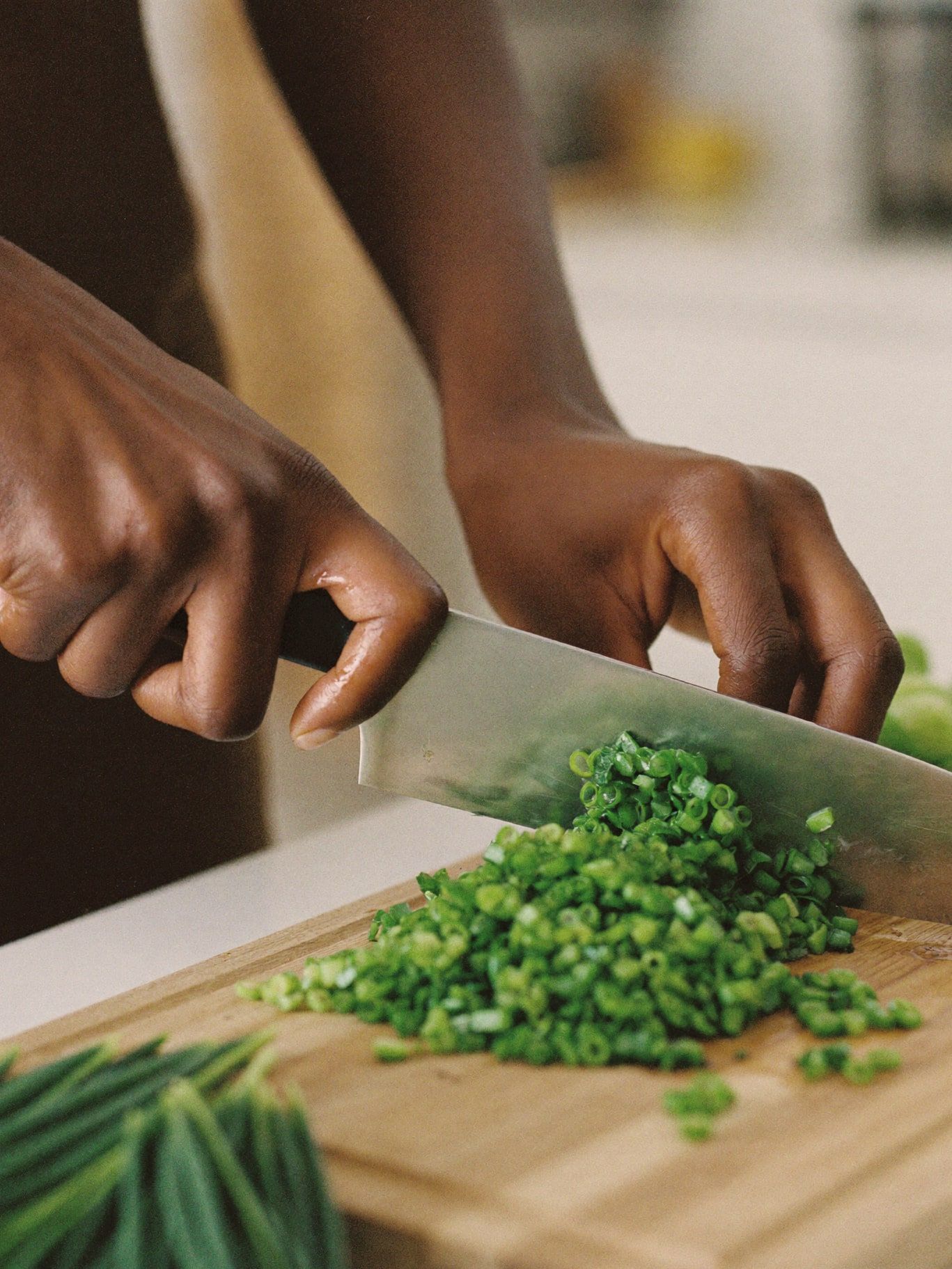 Brown hands chopping fresh leafy greens on a wooden board in a bright kitchen