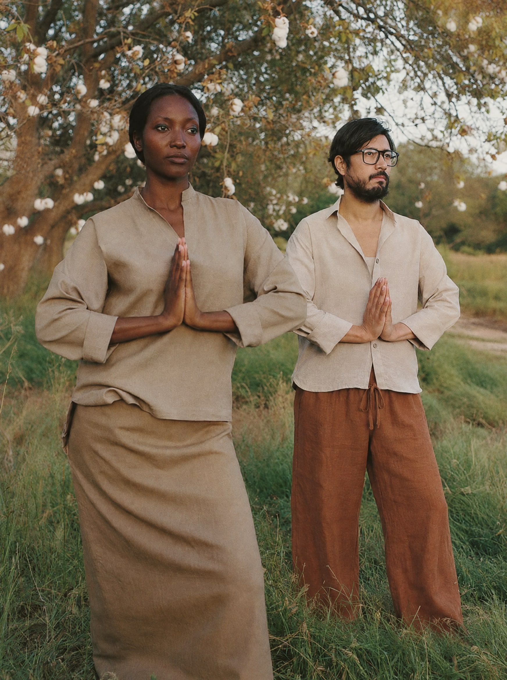 A Black woman and a Chinese American man practicing qi gong in a meadow under cottonwood trees at dawn, in loose long-sleeved linen shirts and linen trousers