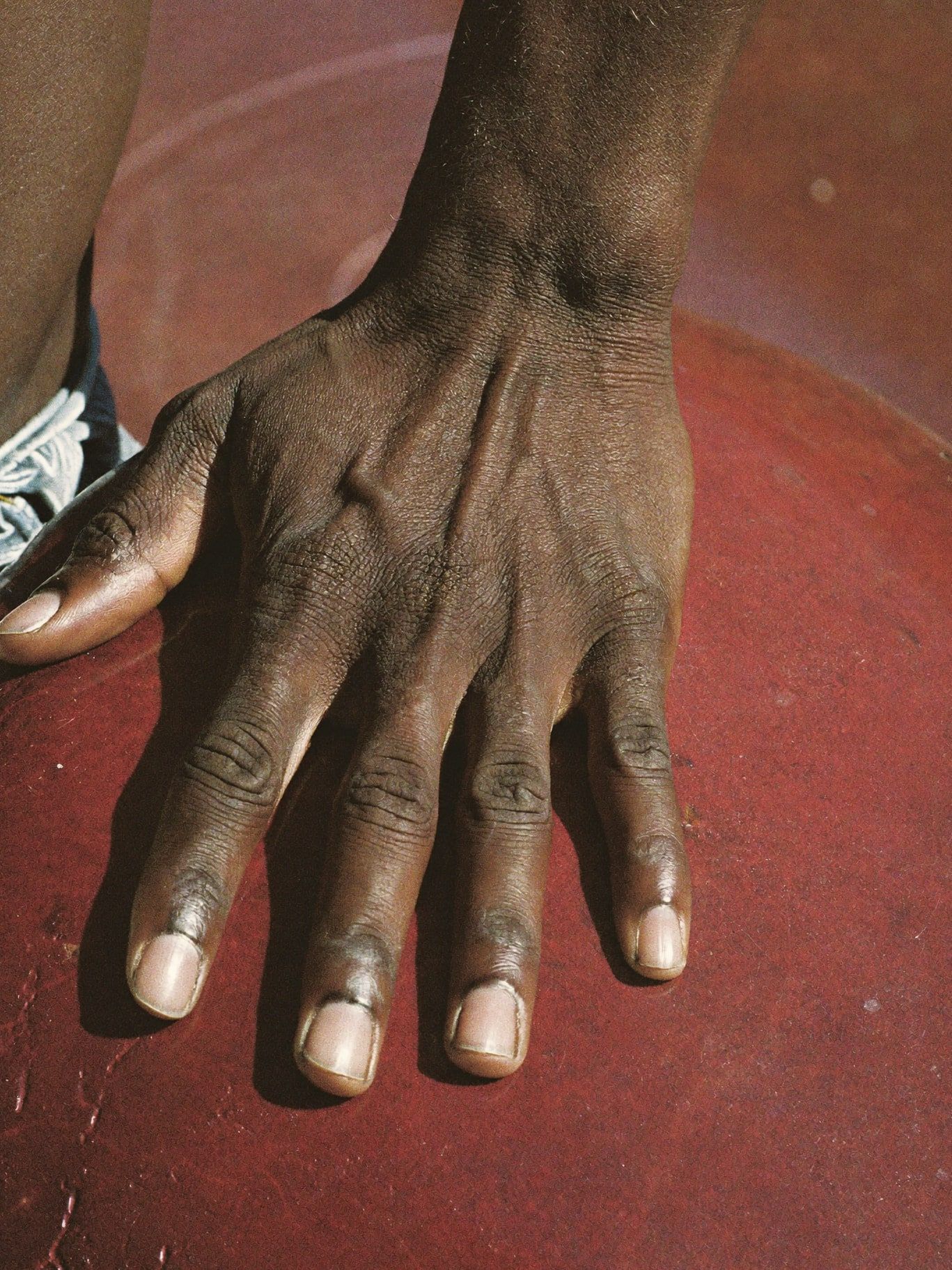 A brown hand resting on a smooth sun-warmed red stone outdoors