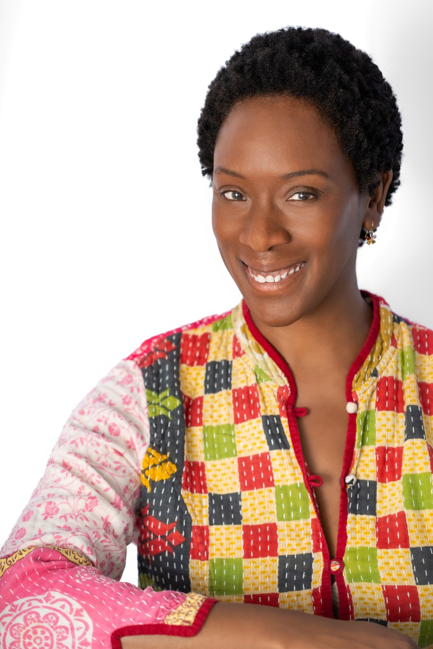Yolessa smiling with her arms crossed, wearing a colorful patchwork jacket